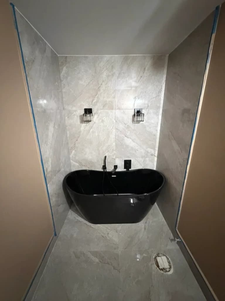 Black freestanding soaking tub with wall-mounted fixtures and large-format tile