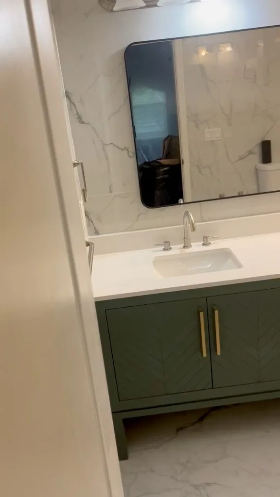 Green bathroom vanity with chevron cabinet fronts beneath a rounded mirror