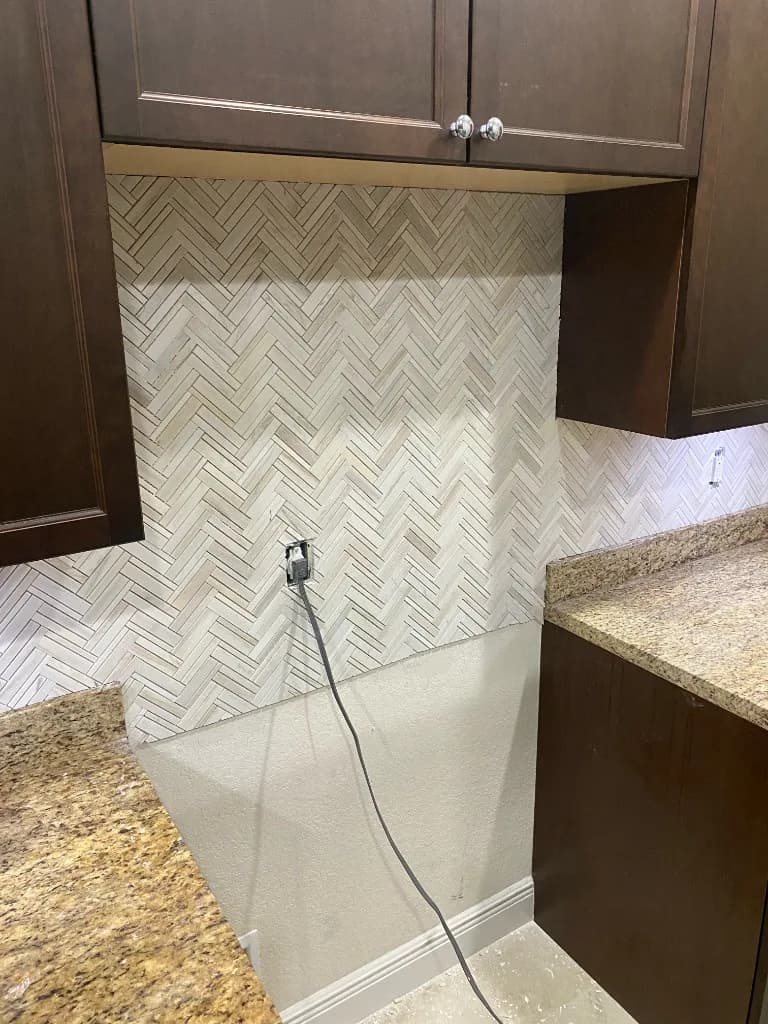 Herringbone stone backsplash installed between dark kitchen cabinets