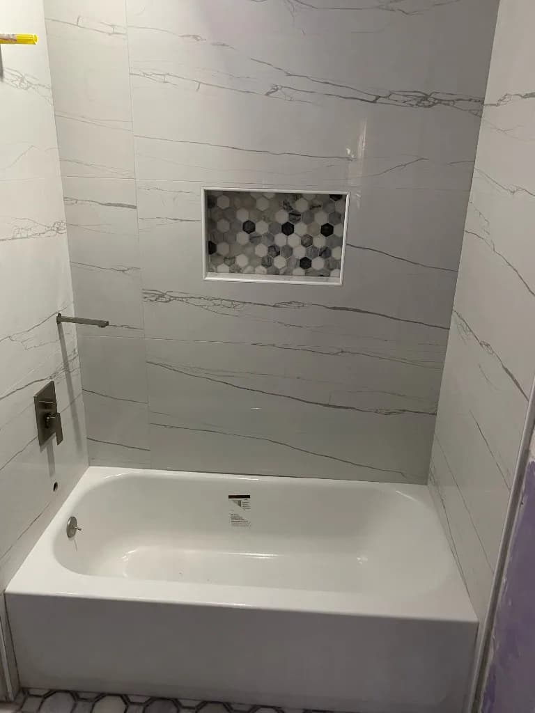 Finished bathtub surround with large-format marble-look tile and a mosaic niche