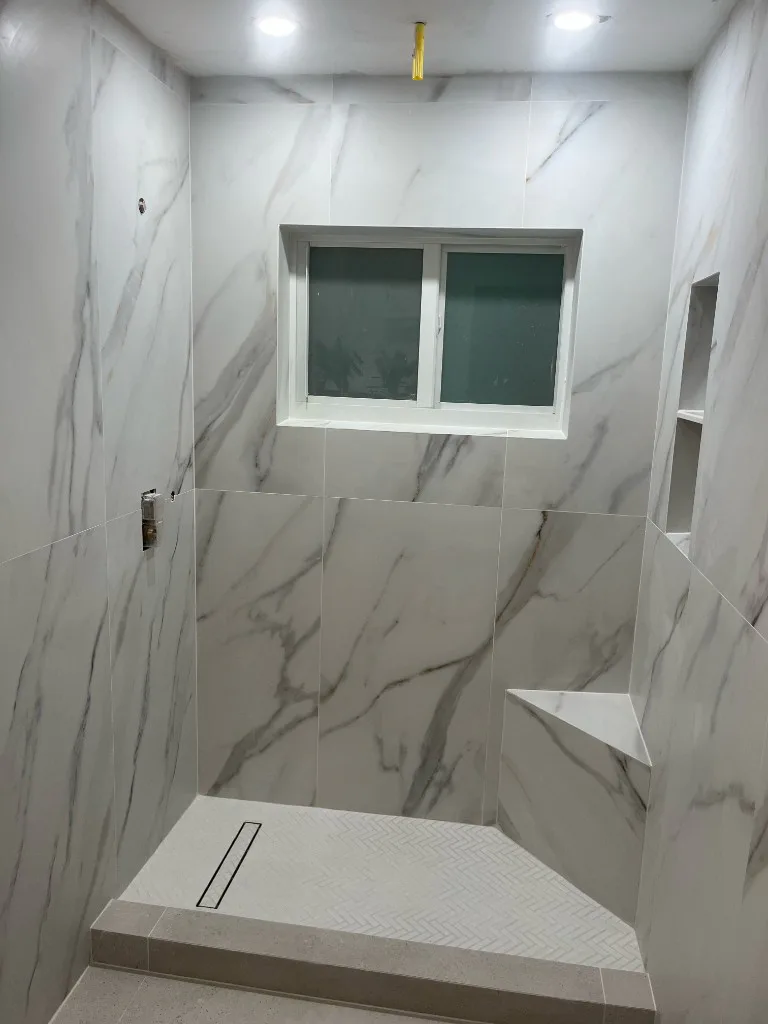 Finished walk-in shower with large-format tile, corner shelves and a linear drain